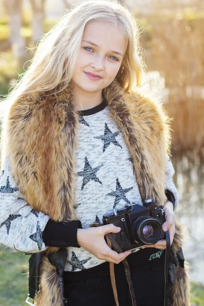 Cute little girl is resting near lake with camera