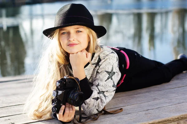 Cute little girl is resting near lake with camera