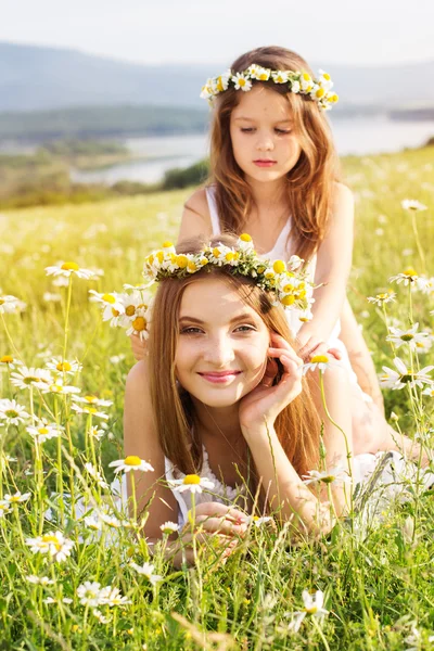 Two pretty girls at meadow with mountain view and flowers