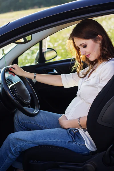 Pregnant happy young woman is sitting in black car