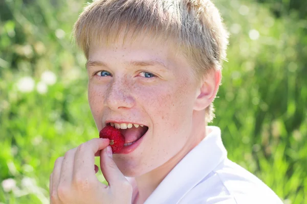 Smiling boy is putting strawberry to his mouth
