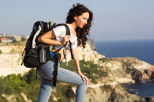 Girl traveler is sitting on rock with backpack