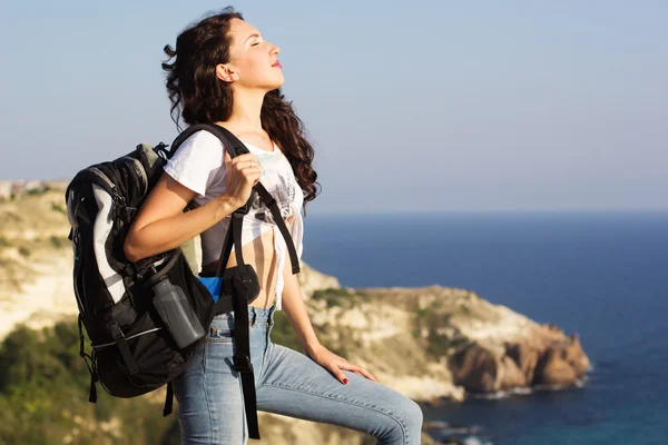 Girl traveler is standing on rock with backpack