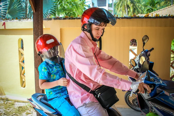 Father and son wearing helmets are going to go on a motorbike in Koh Samui