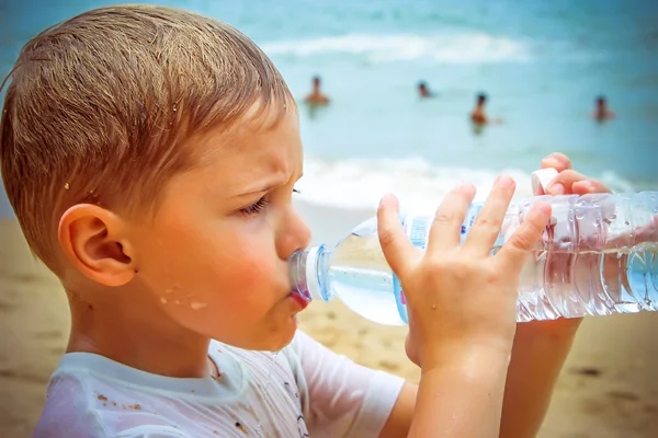 Little boy drinking water on the beach after hard swimming