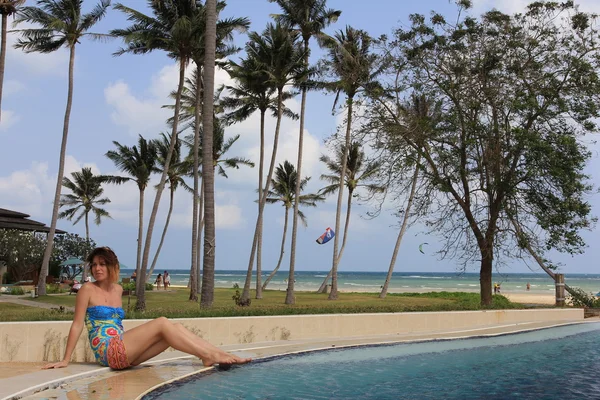 Woman sitting at open-air swimming pool among palm trees