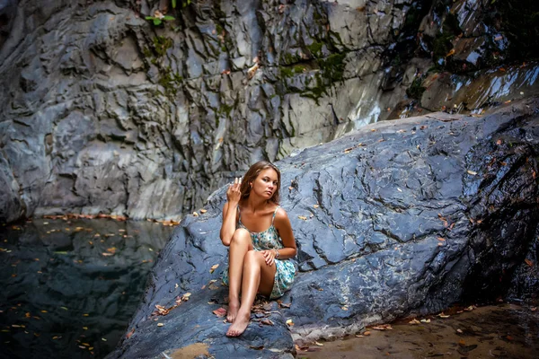 Beautiful girl posing in dress at the waterfall