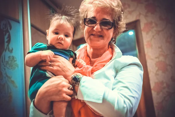 Baby boy in grandmas hands. Woman holding the baby and smiles