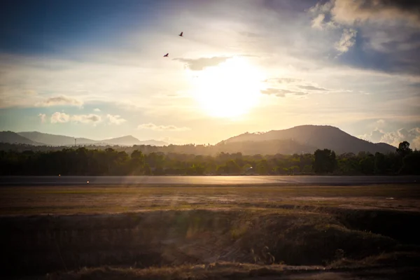 Asphalt road In mountains. Panorama at sunset light with lens flare effects. Birds in the sky. Koh Samui airport