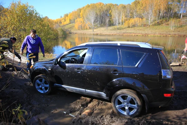 Russia, Siberia, 27 september 2014. SUV got stuck in the mud and trying to go out in the autumn forest. People try to help it