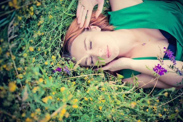 Pensive dreamy attractive young red-haired woman with flowers relaxing outside on a meadow full of flowers.