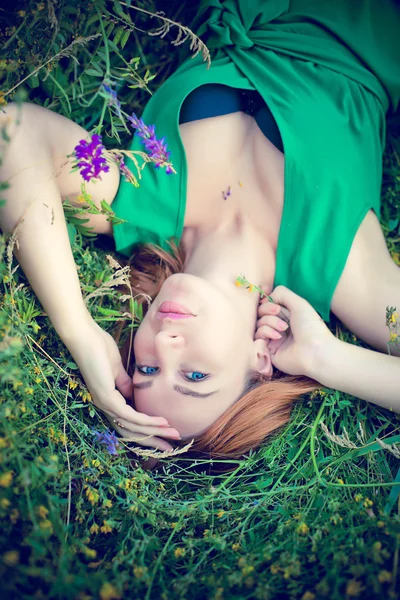 Pensive dreamy attractive young red-haired woman with flowers relaxing outside on a meadow full of flowers.