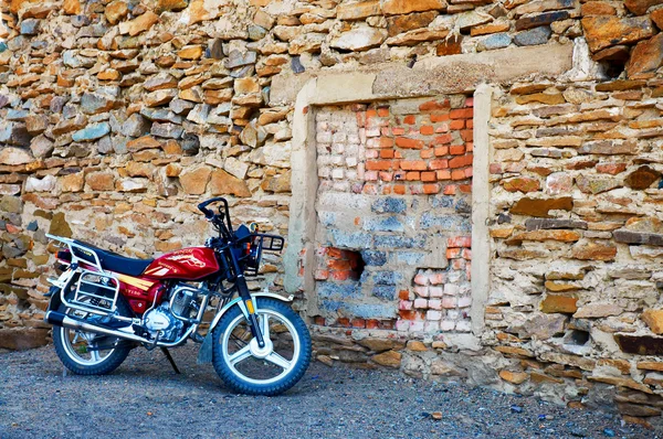 Red motorbike parked near a stone wall