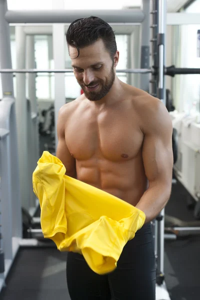 Young strong fit man in gym putting t shirt on