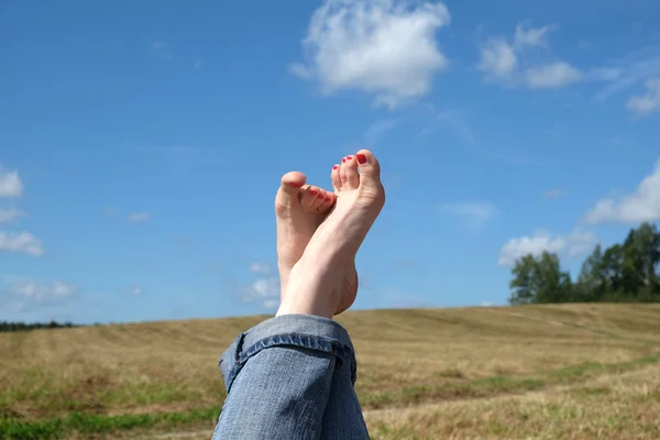 Female bare feet with red nails against summer landscape