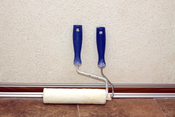 Paint rollers stands in a room at baseboard near the wall