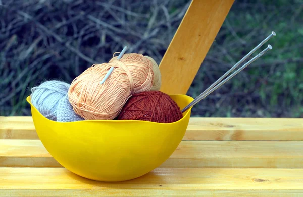 Color skeins of wool yarn, knitting needles and crochet hook in a big yellow bowl