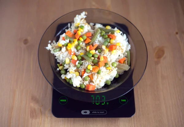 Plate with rise and vegetables on kitchen scales closeup