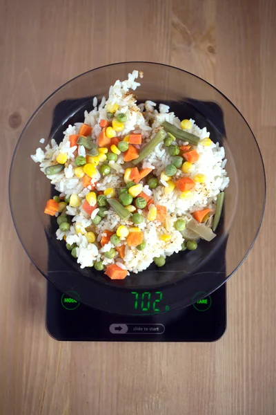 Plate with rise and vegetables on kitchen scales closeup