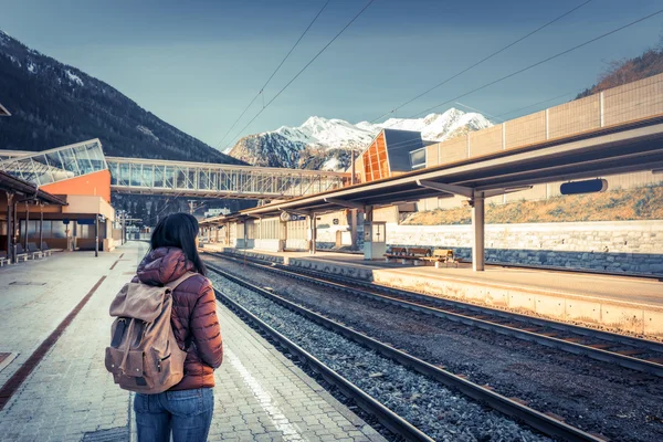 Traveling by train at the Alpine Railroad. Girl waiting train on the platform, in the background snow-capped mountains.