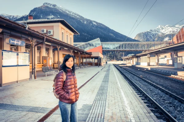 Traveling by train at the Alpine Railroad. Girl waiting train on the platform, in the background snow-capped mountains