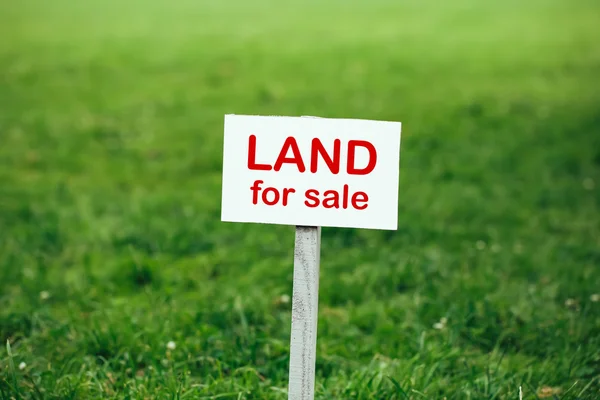 Land for sale sign against trimmed lawn background