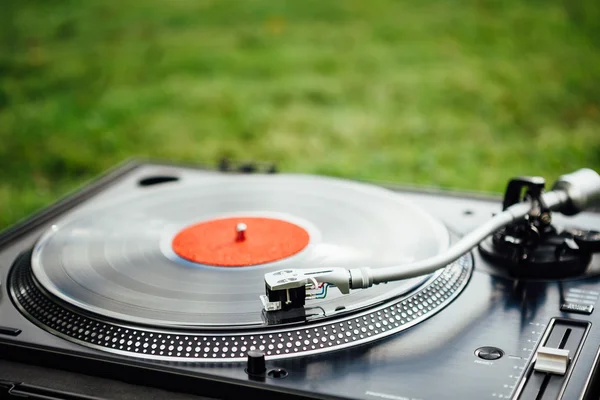 Vinyl disc playing on turntable, green grass background