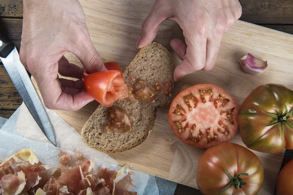 Chef rubbing tomato on a slice of bread