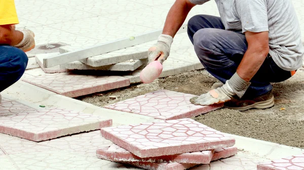 Worker tapping pavers into place with rubber mallets. Installati