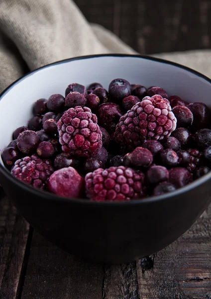 Frozen berries mix in a black bowl on wooden background