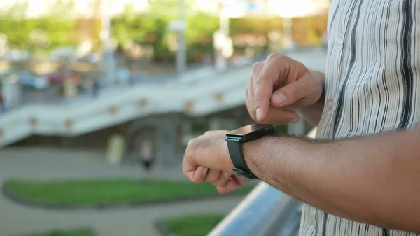 Outdoor portrait of modern young man with smart watch in the street. Against the background  people walking and talking fast city life. Close-up