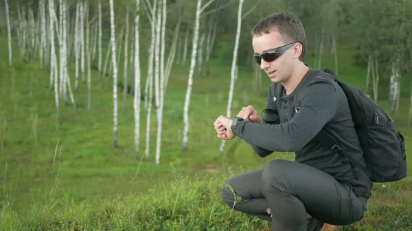 Young man in sunglasses speak in smart watch. Against the background of beautiful nature: green trees and grass