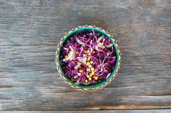 Fresh red cabbage salad with sweet corn in ceramic bowl on rustic wooden table