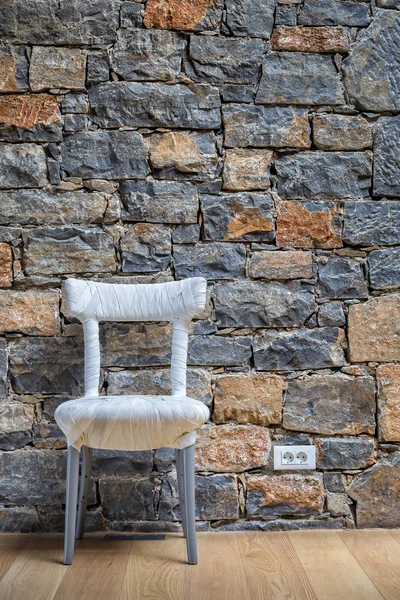 A special chair stands in front of a stone wall