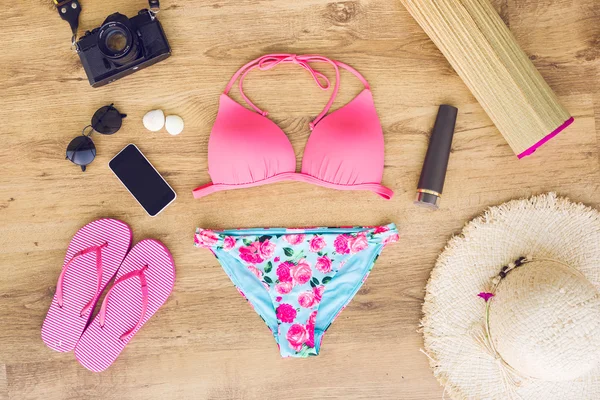 Swimsuit with beach accessories on wood background.