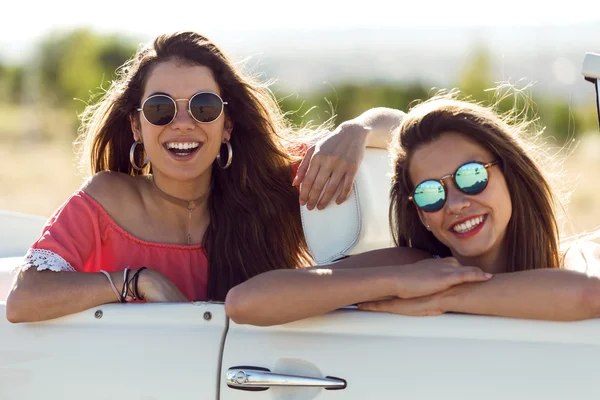 Two pretty young women driving on road trip on beautiful summer