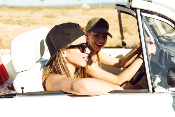 Two pretty young women driving on road trip on beautiful summer