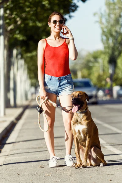 Beautiful young woman with her dog using mobile phone in the str