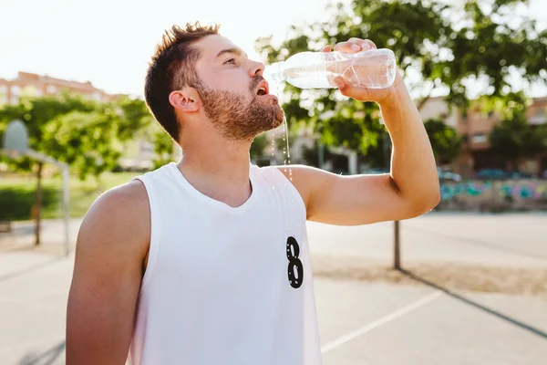 Portrait of handsome young man drinking water on court.