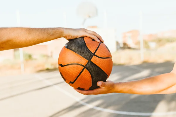 Portrait of two basketball players holding a basket ball on court.