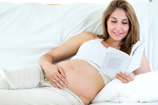 Pregnant woman reading a book on sofa.