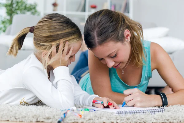 Young mother and daughter drawing on the notebook at home.