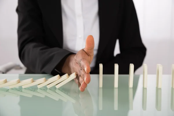 Businesswoman Stopping Dominoes From Falling