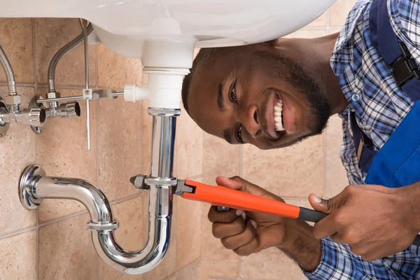 Happy Male Plumber Repairing Sink In Bathroom