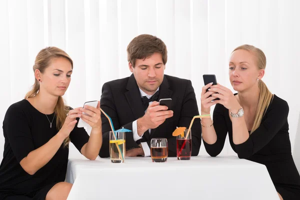Friends Using Mobile Phones In Restaurant