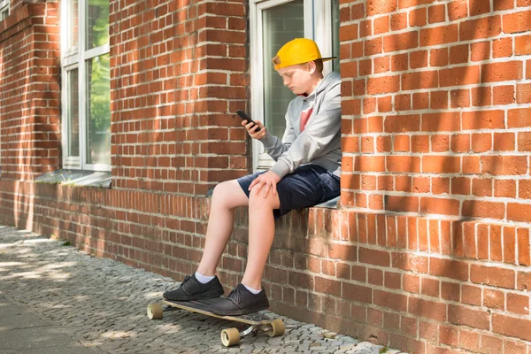 Boy With Skateboard Using At His Mobile Phone