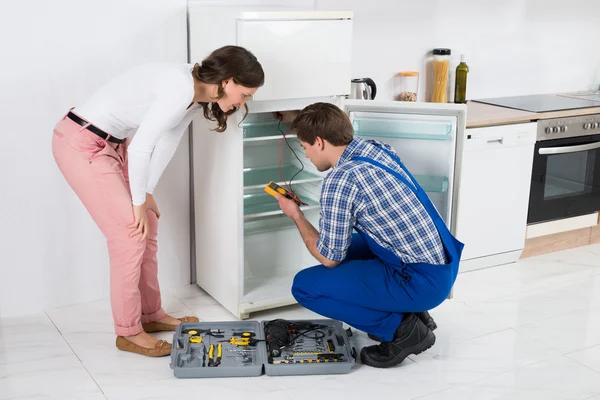 Housewife Looking At Worker Repairing Refrigerator