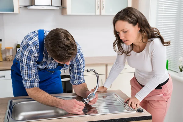 Woman Looking At Plumber Fixing Steel Tap