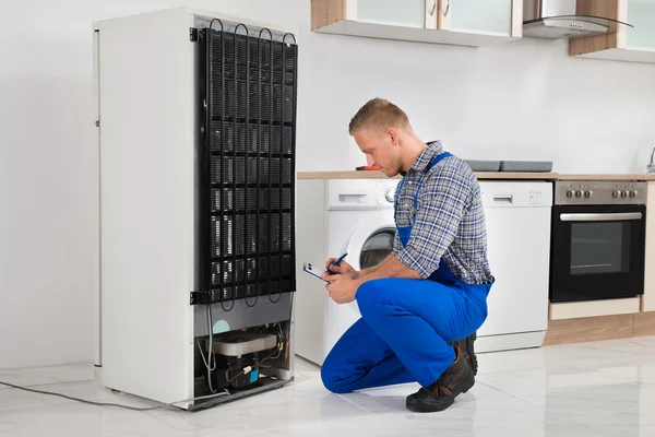 Plumber Writing On Clipboard In Front Of Refrigerator