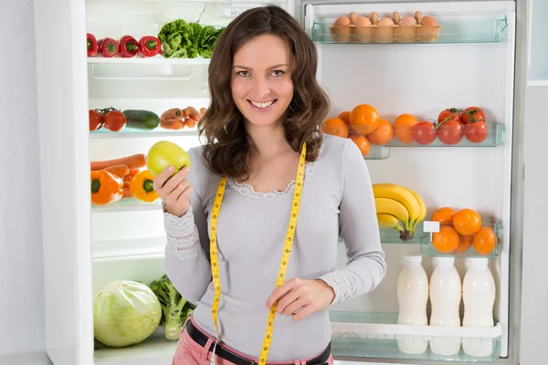 Woman With Measuring Tape And Apple Near The Refrigerator